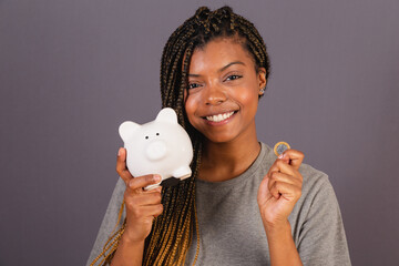 Young afro brazilian woman holding piggy bank and coin, concept of economy, finance, saving.