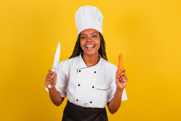 Young afro brazilian woman, chef cook, holding knife and carrot, for peeling and chopping.