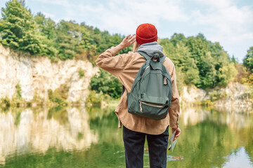 Back view of stylish hipster woman wearing backpack, red hat looking at mountain lake view while relaxing in nature. Relax time on holiday concept travel 