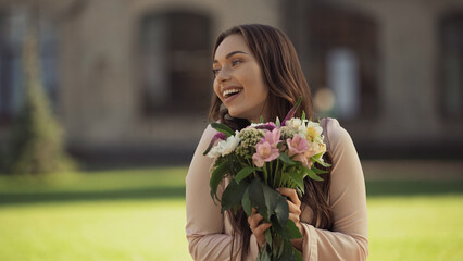 Positive young woman smiling while holding flowers in park.