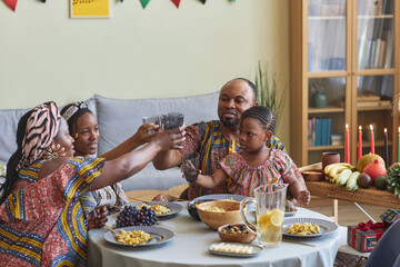African family in national costumes toasting with drinks sitting at dining table, they celebrating...
