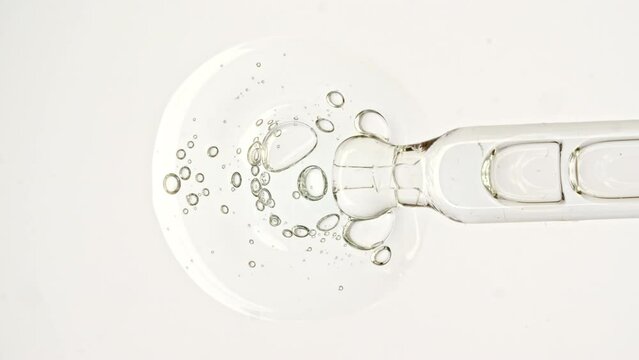 Transparent cosmetic gel fluid, serum with molecule bubbles oil in pipette drips on a white background. Macro Shot of Natural Organic Cosmetics, Medicine. Production Close-up. Slow Motion. 4k