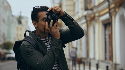 Bi-racial traveler with backpack taking photo on vintage camera on urban street.