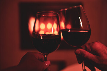 Couple making a toast with glasses of red wine. Fireplace background - Christmas mood.