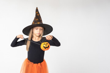 Kids Halloween. A beautiful cute girl in a witch costume, a hat, holding Jack's lantern, conjuring...