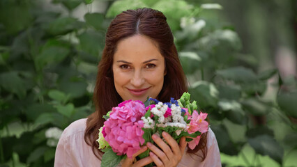 Cheerful brunette woman looking at camera and holding flowers in park.
