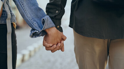Cropped view of multiethnic couple holding hands on urban street.
