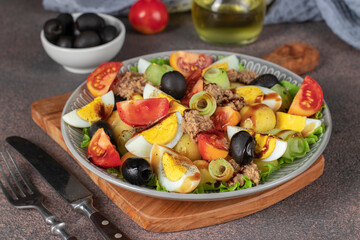 French salad Nicoise with tuna, boiled potatoes, egg, black olives, cucumbers, tomatoes and lettuce poured balsamic sauce