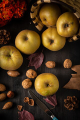 overhead view of pippin apples with nuts, autumn leaves, orange flowers, basket and knife on wooden table, vertical