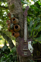 Cantaritos de barro viejos guitarra eléctrica vieja desgastada colgados sobre árbol de jardín   