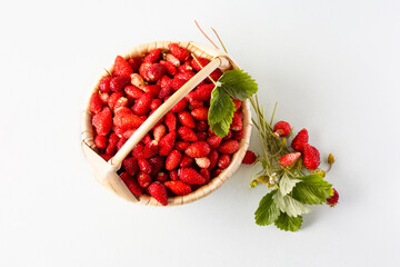 Wild strawberries in a beige basket on a gray background with green leaves, healthy and delicious food