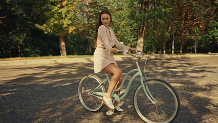 Smiling woman in dress riding bicycle in summer park.