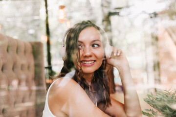 Portrait of a beautiful young woman with headphones, who listens to music while sitting in a street cafe.Enjoy the music, generation Z