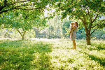 Fototapeta na wymiar The joy of motherhood. Mom and daughter in the cherry orchard. Sunbeams on a green meadow