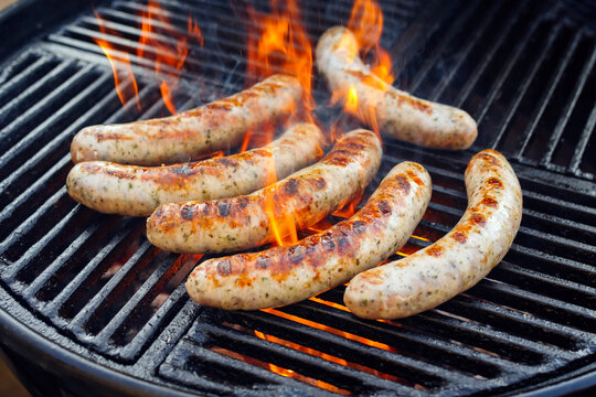 Rohe grobe gegrillte Allg&auml;uer Bratwurst angeboten als close-up auf einem Holzkohlegrill mit Feuer und Rauch