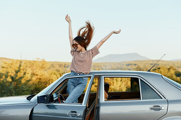 Happy woman traveler climbed on the car and spread her arms smiling happily. looks at the nature...