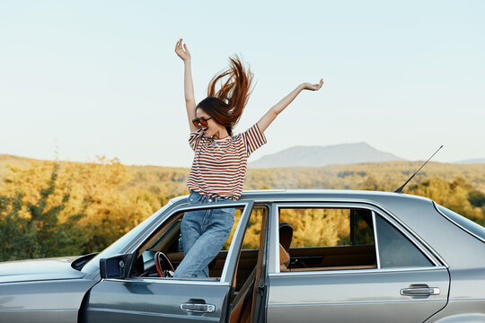 Happy woman traveler climbed on the car and spread her arms smiling happily. looks at the nature around. Lifestyle in travel and joy