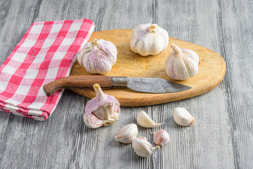 some garlic cloves on a cutting board next to a knife and a kitchen rag

