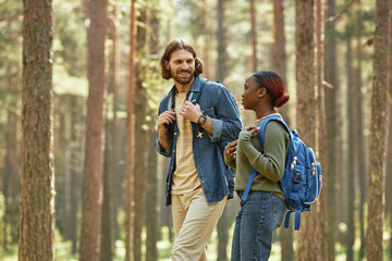 Fototapeta premium Multiethnic young couple with backpacks walking together in the forest outdoors