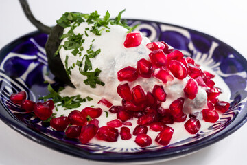 Delicioso Chile en Nogada en plato de talavera azul sobre fondo blanco.