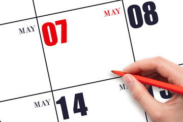 A hand holding a red pen and pointing on the calendar date May 7. Red calendar date, copy space,...