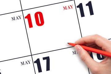 A hand holding a red pen and pointing on the calendar date May 10. Red calendar date, copy space,...