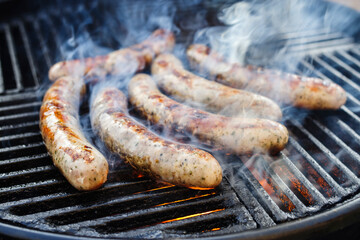 Gegrillte Allgäuer Bratwurst angeboten als close-up auf einem Holzkohlegrill mit Feuer und Rauch
