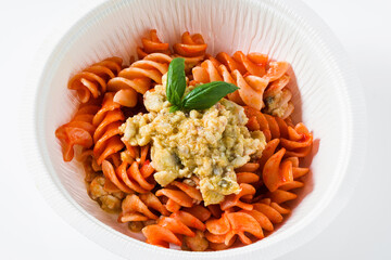 fusilli pasta in tomato sauce with rabbit sauce and fresh basil in a plastic takeout container