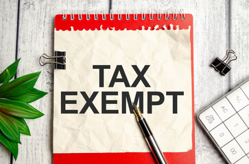 tax exempt , text on white paper and red notepad on wooden background