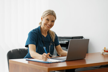 Female healthcare worker doing some paperwork and using laptop while working at doctor's office