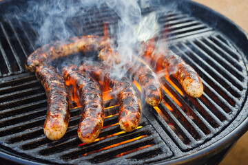 Barbecue Allgäu bratwurst offered as close-up on a charcoal grill with fire and smoke