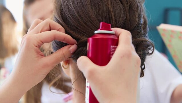 Close-up on the hairstyle of a girl, a hairdresser splashes hairspray. The master makes a haircut for a woman client. Business concept, beauty salon. Barber hair care. UHD 4K.