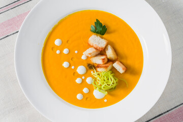 carrot puree soup with croutons and leeks in a plate on a linen tablecloth