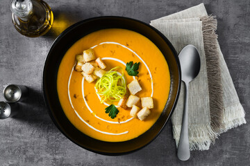 carrot puree soup with croutons and leeks on a dark background