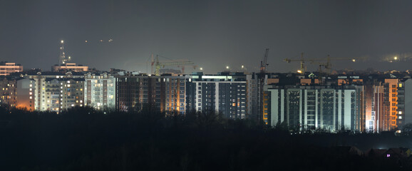 Dark silhouette of tower cranes at high residential apartment buildings construction site at night....