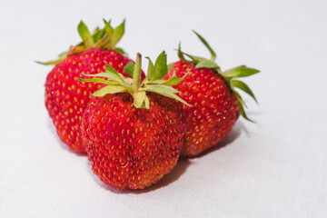 Red berry juicy strawberry. Three ripe strawberries with strawberry leaf, isolated on a white fabric background. Healthy eating and food concept