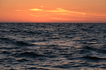 Obraz premium Dramatic bright red sky at ocean sunset, soft evening clouds over sea dark water