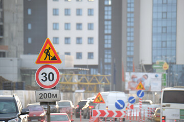 Roadworks warning traffic signs of construction work on city street and slowly moving cars