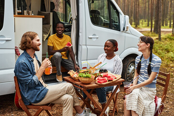 Young friends having lunch at table at picnic in the forest, they travelling on house of wheels
