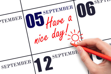 The hand writing the text Have a nice day and drawing the sun on the calendar date September  5