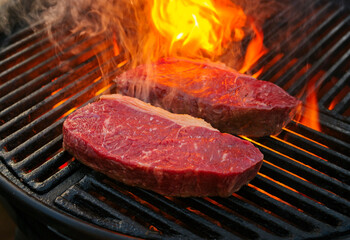 Raw dry aged wagyu roast beef steak grilled as close-up on a charcoal grill with fire and smoke