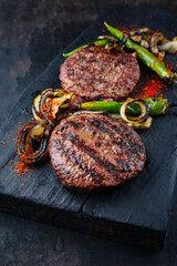 Barbecue wagyu beef Hamburger with grilled chili and onion rings served as close-up on a charred wooden board