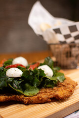 Milanese with topping. Milanesa covered with arugula, tomatoes, cheese. Breaded meat. Italian food. Fried meat. Beef, chicken meat, pork meat.