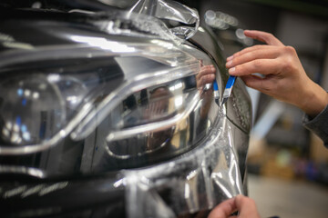 The process of installing PPF on the headlight of the car. PPF is a protective film for paint that protects the paint from scratches and stone chips. The concept of car body protection. Wrap.  - obrazy, fototapety, plakaty