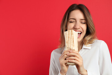 Young woman eating delicious shawarma on red background, space for text