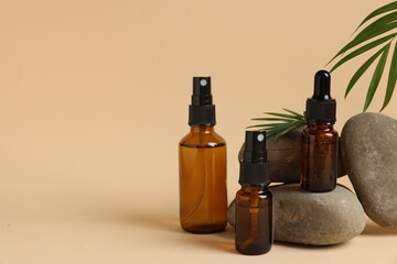 Bottles of organic cosmetic products, green leaf and stones on beige background, space for text