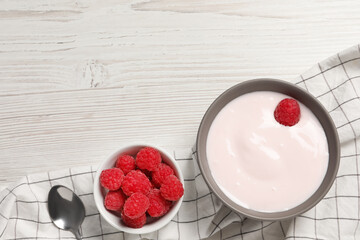 Bowl of tasty yogurt served with raspberries on white wooden table, flat lay. Space for text