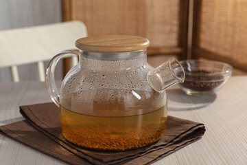 Glass teapot with aromatic buckwheat tea and granules on wooden table