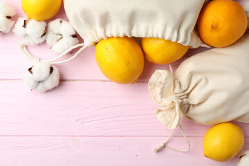 Cotton eco bags with citrus fruits on pink wooden table, flat lay