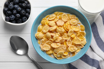 Bowl of tasty corn flakes and blueberries served for breakfast on white wooden table, flat lay